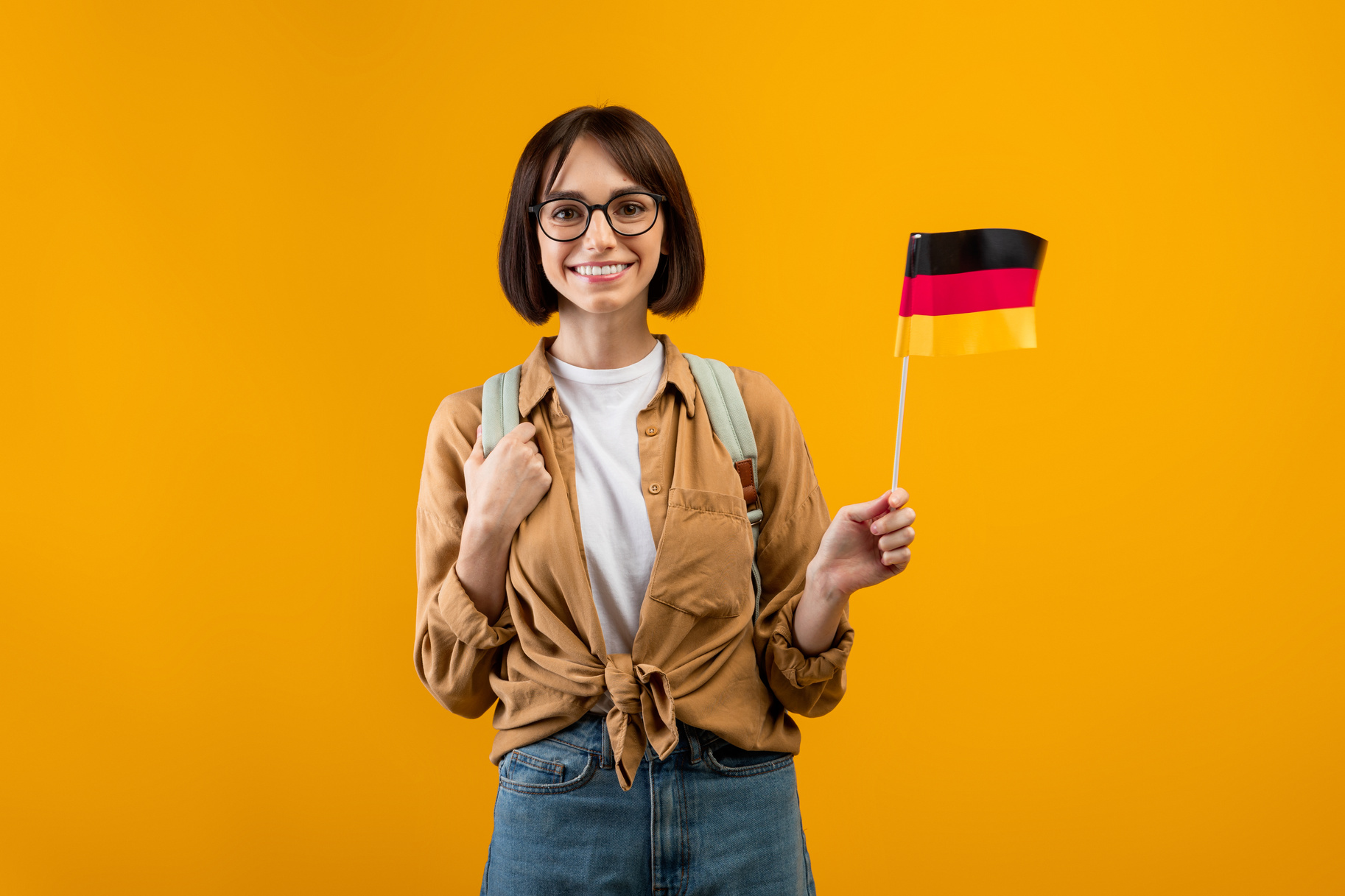 Education Abroad, Studying in Germany Concept. Happy Young Student in Glasses with Backpack Holding Flag of Germany